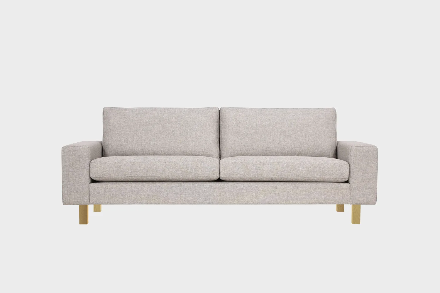 Vaalean beige 3n istuttava Studio XL -sohva tammen värisillä jaloilla kuvattuna suoraan edestäpäin vaaleaa taustaa vasten.