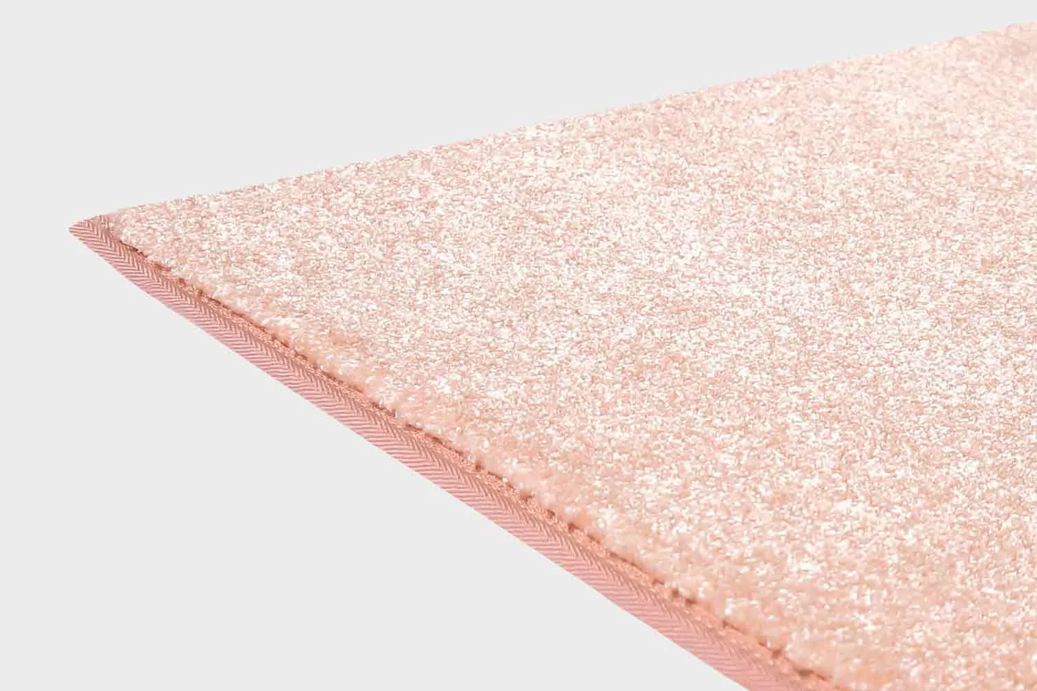 Rosan värinen VM Carpet Hattara matto. Lähikuva maton kulmasta, josta näkyy kanttaus ja maton materiaali.
