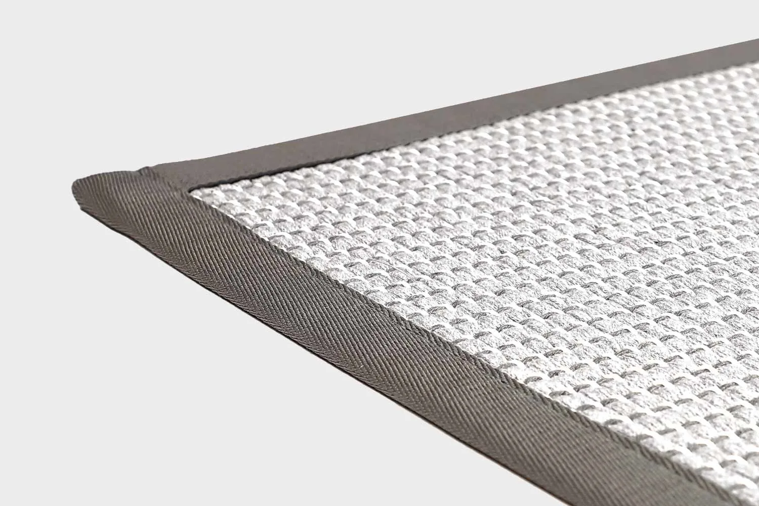Vaaleanharmaa VM Carpet Lyyra 2 matto. Lähikuva maton kulmasta, josta näkyy kanttaus ja maton materiaali.