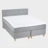 comfy-jenkkivuode-180x200cm-cosmo110-tammi-finsoffat Harmaa 180 cm leveä ja 200 cm pitkä jenkkisnäky napillisella sängynpäädyllä ja tammen värisillä kantikkailla puujaloilla.
