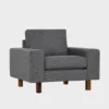studio-xl-lepotuoli-100x90-das52darkgrey-pahkina-finsoffat Tummanharmaa kangasverhoiltu nojatuoli pähkinän värisillä jaloilla. Tuolissa on leveät käsinojat ja se on asetettu viistosti vaalean harmaata taustaa vasten.