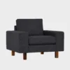 studio-xl-lepotuoli-100x90-das55black-pahkina-finsoffat Musta kangasverhoiltu nojatuoli pähkinän värisillä jaloilla. Tuolissa on leveät käsinojat ja se on asetettu viistosti vaalean harmaata taustaa vasten.