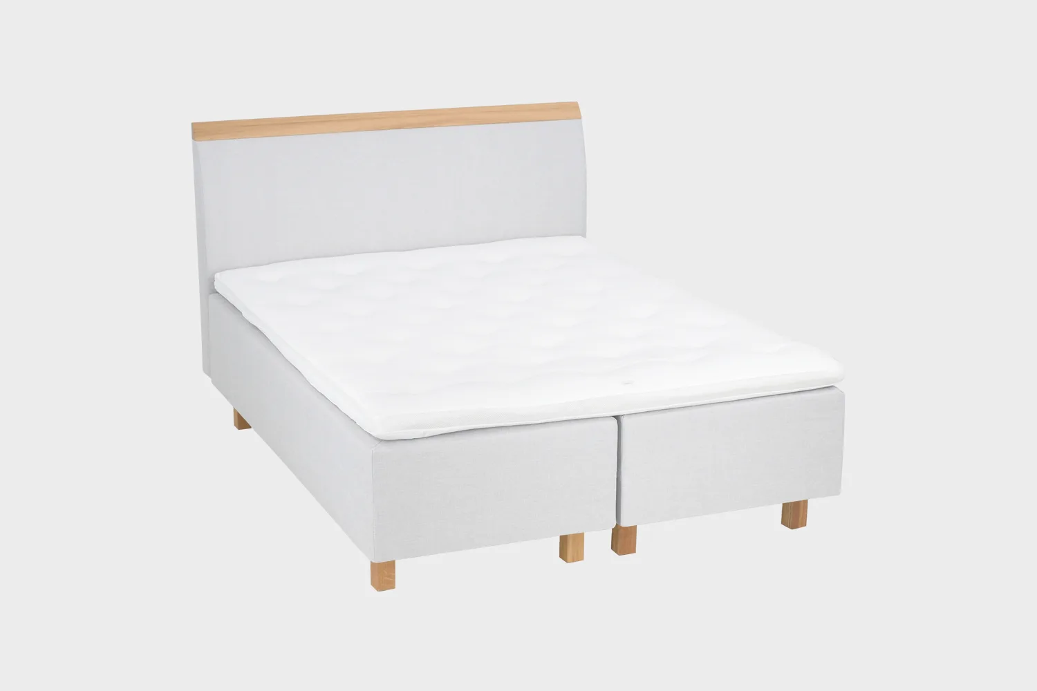 savoy-comfort-runkopatjasanky-180x200cm-das50-tammi-finsoffat Vaaleanharmaa runkosänky 180x200 cm tammen värisillä jaloilla ja vaaleanharmaalla sängynpäädyllä, jossa tammen värinen puukoristelista yläosassa. Kuvattuna viistosti vaaleanharmaata taustaa vasten.