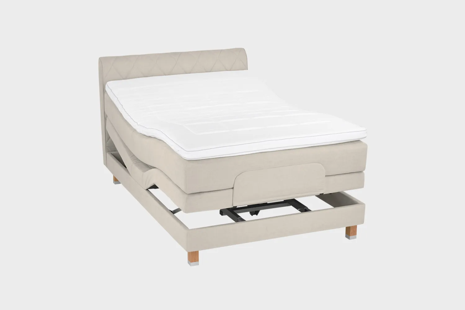 Vaalean beige moottorisänky koossa 140x200 cm tammen värisillä jaloilla sekä samanvärisellä sängynpäädyllä. Sänky on kuvattuna viistosti kumpikin pääty aavistuksen koholla vaaleaa taustaa vasten.